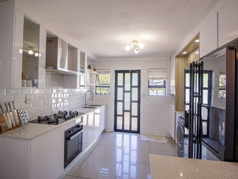 Modern, well-appointed kitchen featuring sleek white gloss cabinetry, stone countertops, subway tile backsplash, and integrated gas hob and oven.
