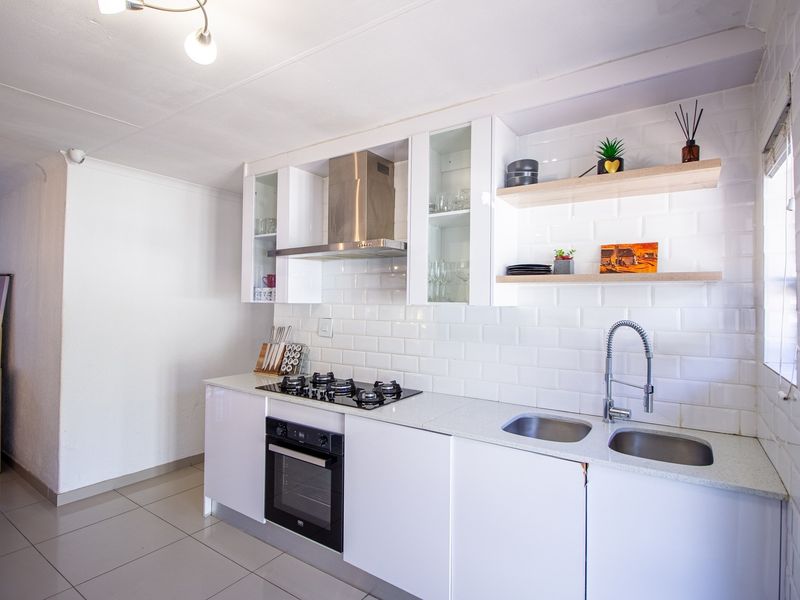 Modern kitchen featuring white cabinetry, subway tile backsplash, stone countertops, gas hob, built-in oven, and floating timber shelving.