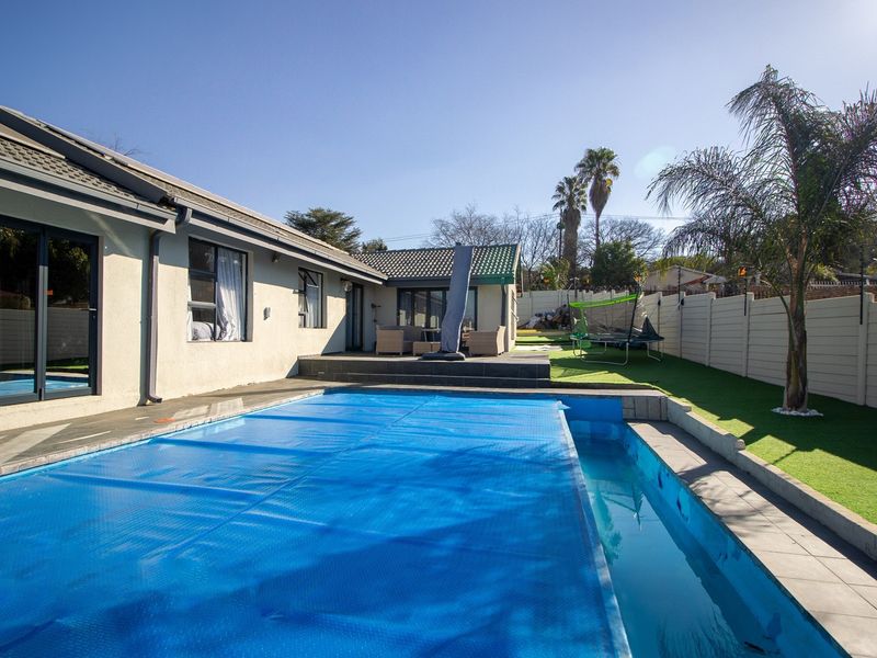 A well-maintained outdoor pool area featuring a blue pool cover, tiled surround, and direct access to the home via sliding glass doors.