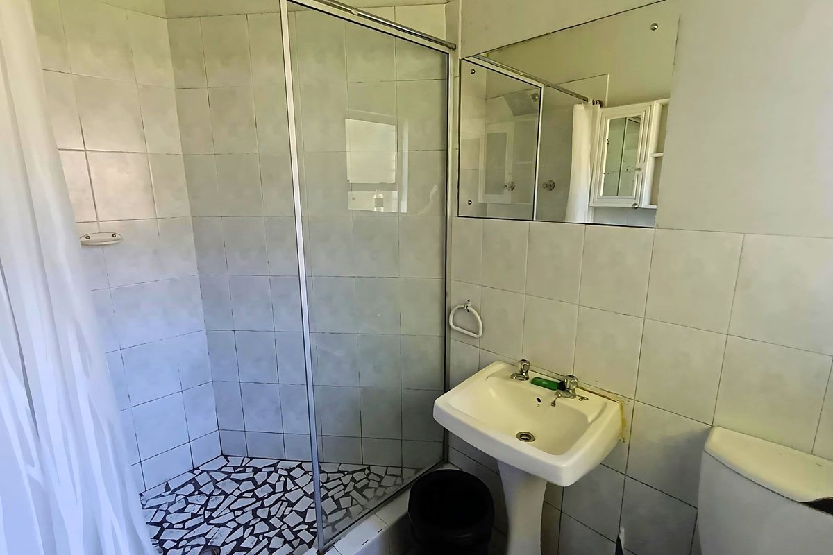 A compact bathroom featuring a corner shower enclosure with glass door, a pedestal basin, and wall-mounted mirror.