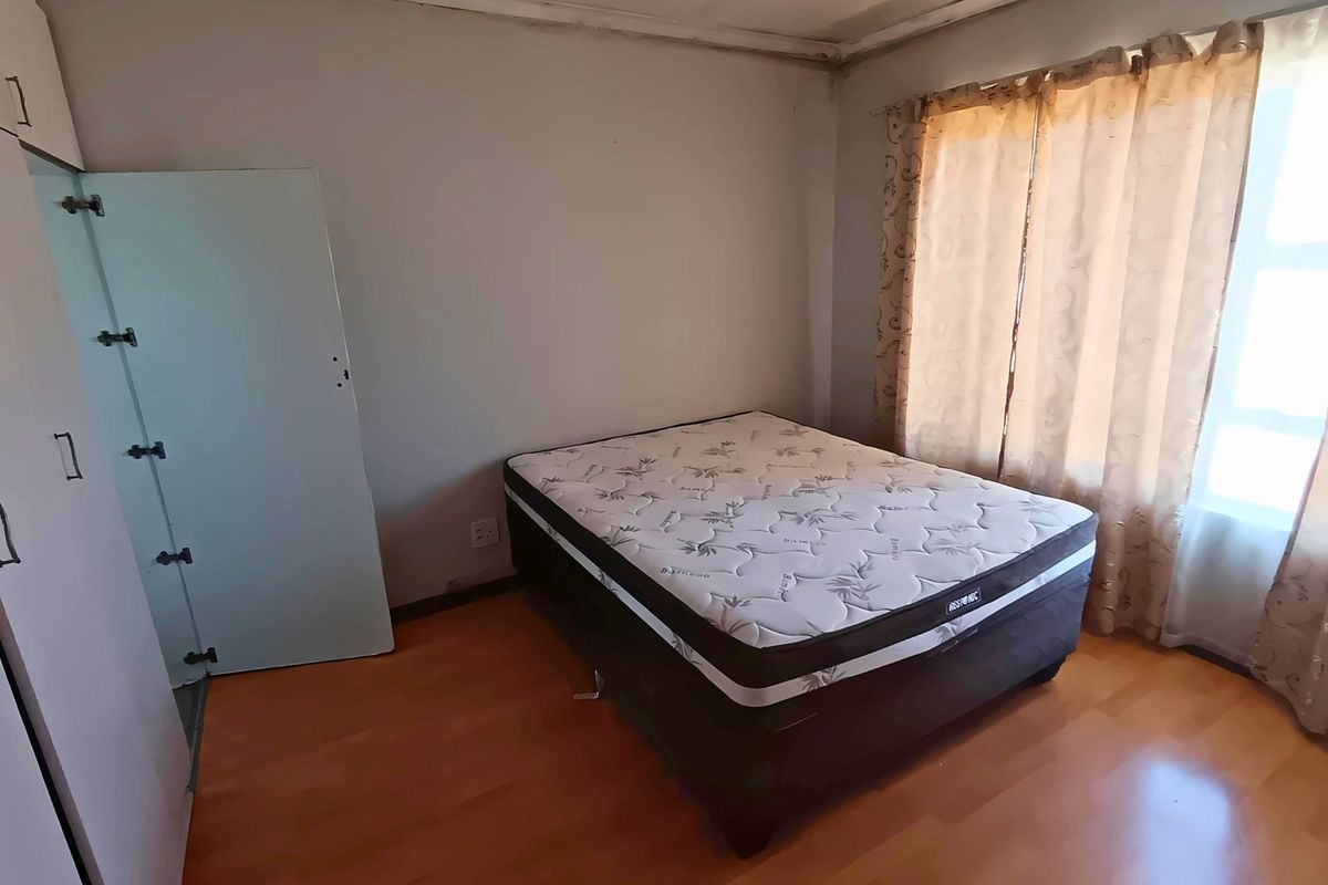A bedroom featuring laminate flooring, built-in cupboards, and large windows with curtains.