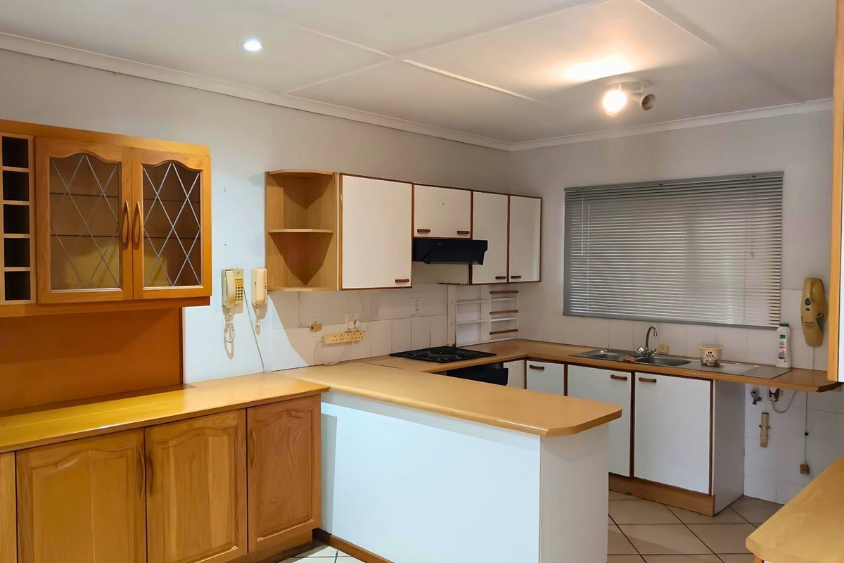 A functional kitchen featuring a breakfast bar, built-in cabinetry, a hob, and a double sink with tiled flooring and window blinds.