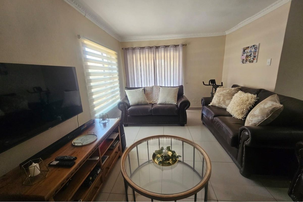 A comfortable living room featuring tiled flooring, decorative ceiling cornices, and dual window treatments including roller blinds and curtains.
