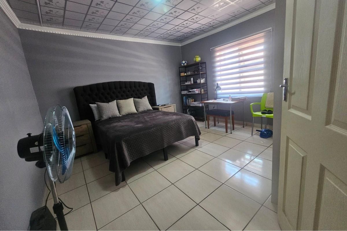 A bedroom featuring tiled flooring, a decorative ceiling finish, and a window with fitted blinds.