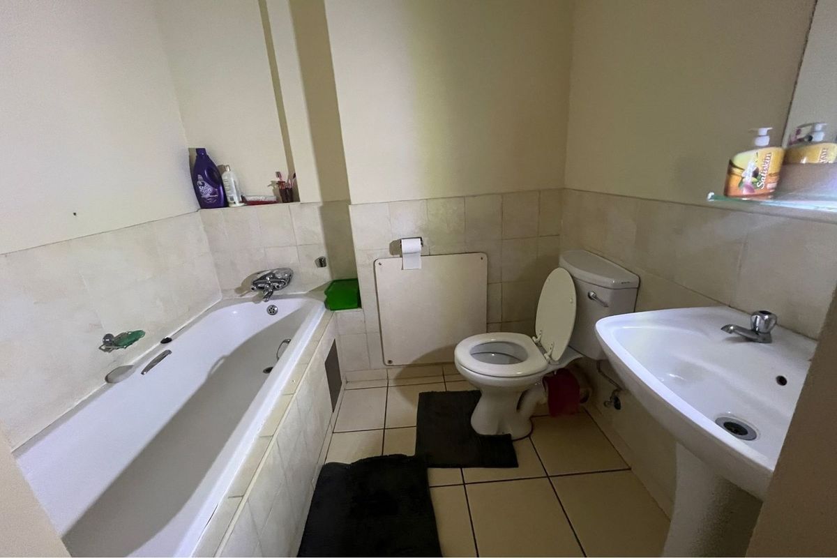 A functional bathroom featuring a standard bathtub, pedestal sink, and toilet with neutral wall tiling and floor tiles.