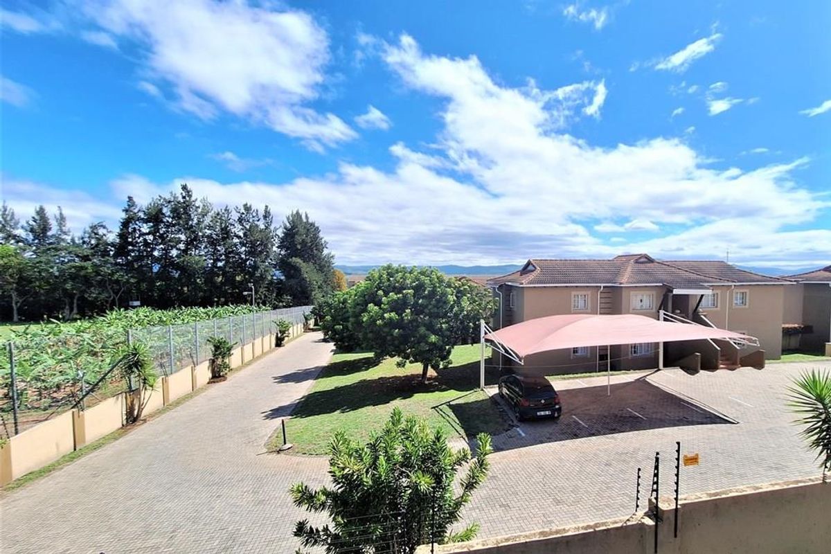 Elevated view of the apartment complex grounds, featuring paved parking areas, shade-cloth carports, landscaped garden space, and perimeter security fencing.