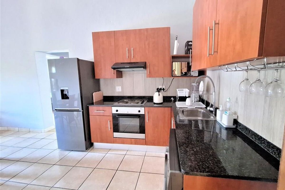A functional kitchen featuring wood-finish cabinetry, dark granite countertops, a built-in oven, hob, extractor fan, and a stainless steel sink.