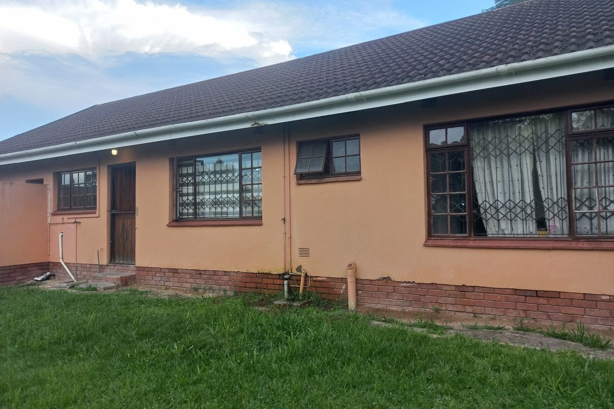 Rear exterior view of the house featuring a tiled roof, brick base, and security-fitted windows with visible signs of exterior wear.