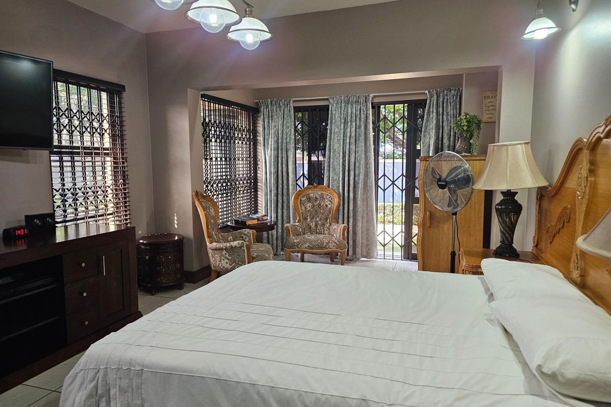 A spacious bedroom featuring tiled flooring, built-in lighting, and large sliding glass doors with security gates leading to the exterior.