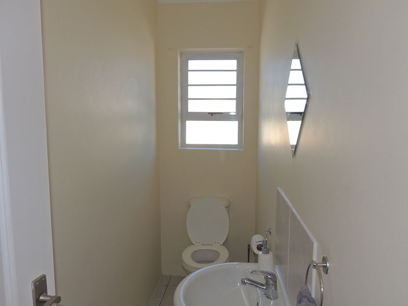 A compact guest bathroom featuring a standard toilet, pedestal basin, and a small window for natural light.