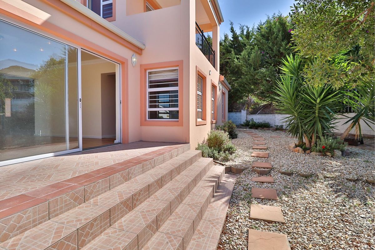 Rear exterior view featuring a tiled patio with steps leading to a low-maintenance gravel garden with established shrubs and a stone pathway.