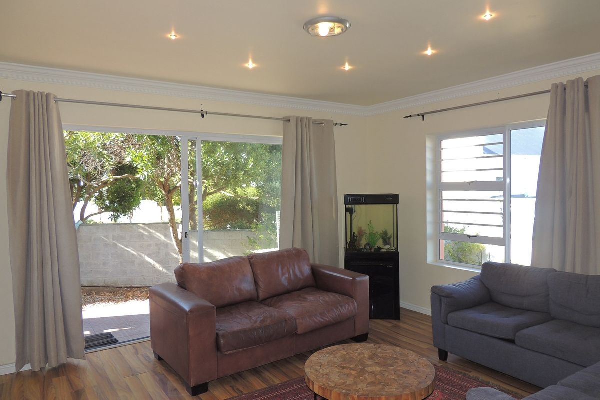 A bright living room featuring wood-look flooring, recessed ceiling lighting, and large sliding glass doors providing direct access to the outdoor area.