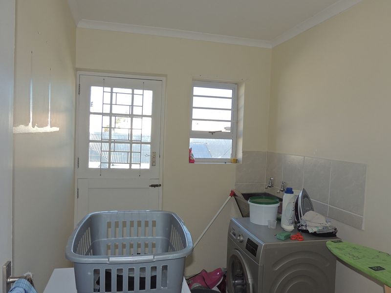 Functional laundry room featuring tiled splashback, plumbing connections for appliances, and direct access to the exterior via a security-fitted door.