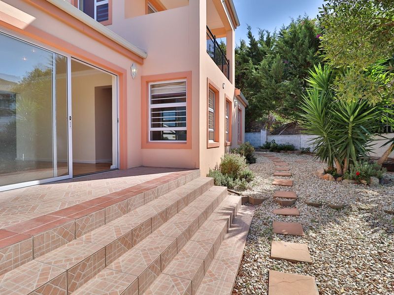 Rear exterior view featuring a tiled patio with steps leading to a low-maintenance gravel garden with established shrubs and a stone pathway.