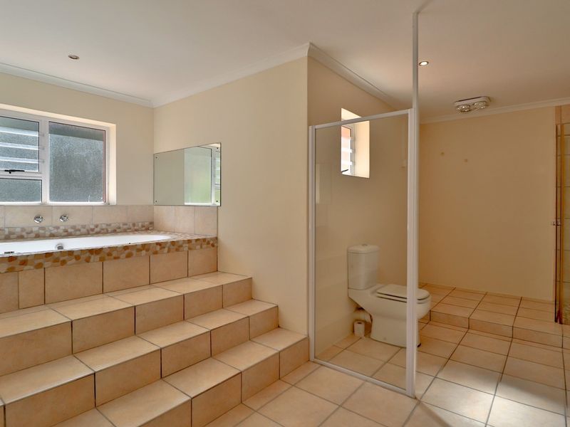 Spacious bathroom featuring a raised tiled bathtub, a separate glass-enclosed shower, and a toilet, finished with neutral wall tones and ceramic floor tiles.