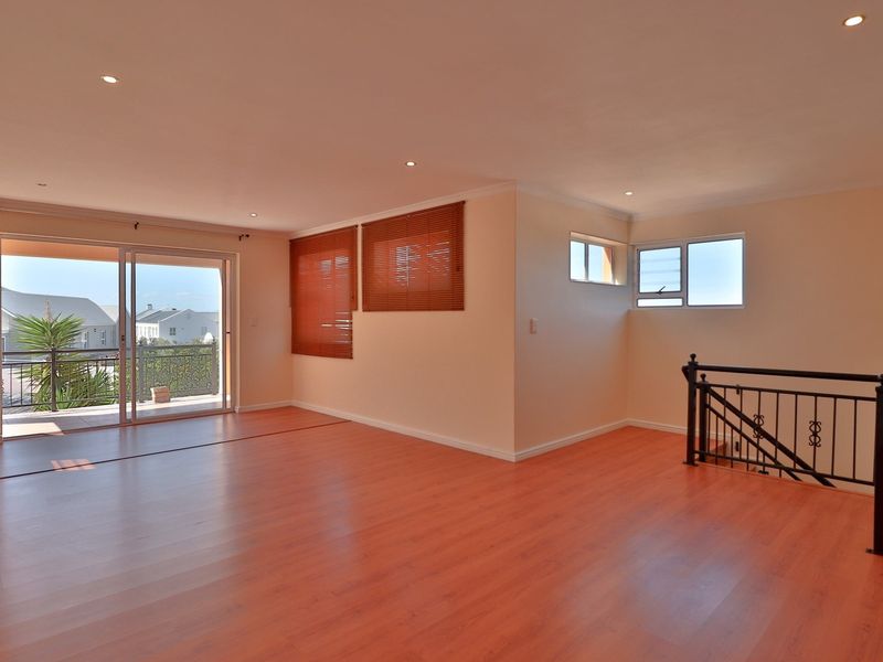 Spacious open-plan living area featuring laminate flooring, recessed lighting, and sliding glass doors leading to a balcony with a metal balustrade.
