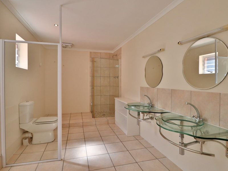 Spacious bathroom featuring a double vanity with glass vessel sinks, a separate glass-enclosed shower, and a private toilet area.