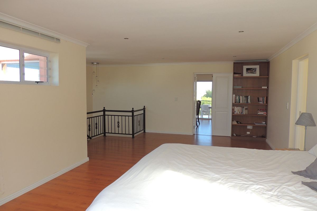 Spacious bedroom featuring laminate flooring, built-in shelving, and a metal balustrade, with direct access to an adjoining room and balcony.