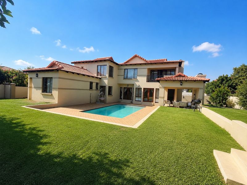 Rear view of a two-story house featuring a swimming pool, paved patio area, balcony, and well-maintained garden lawn.