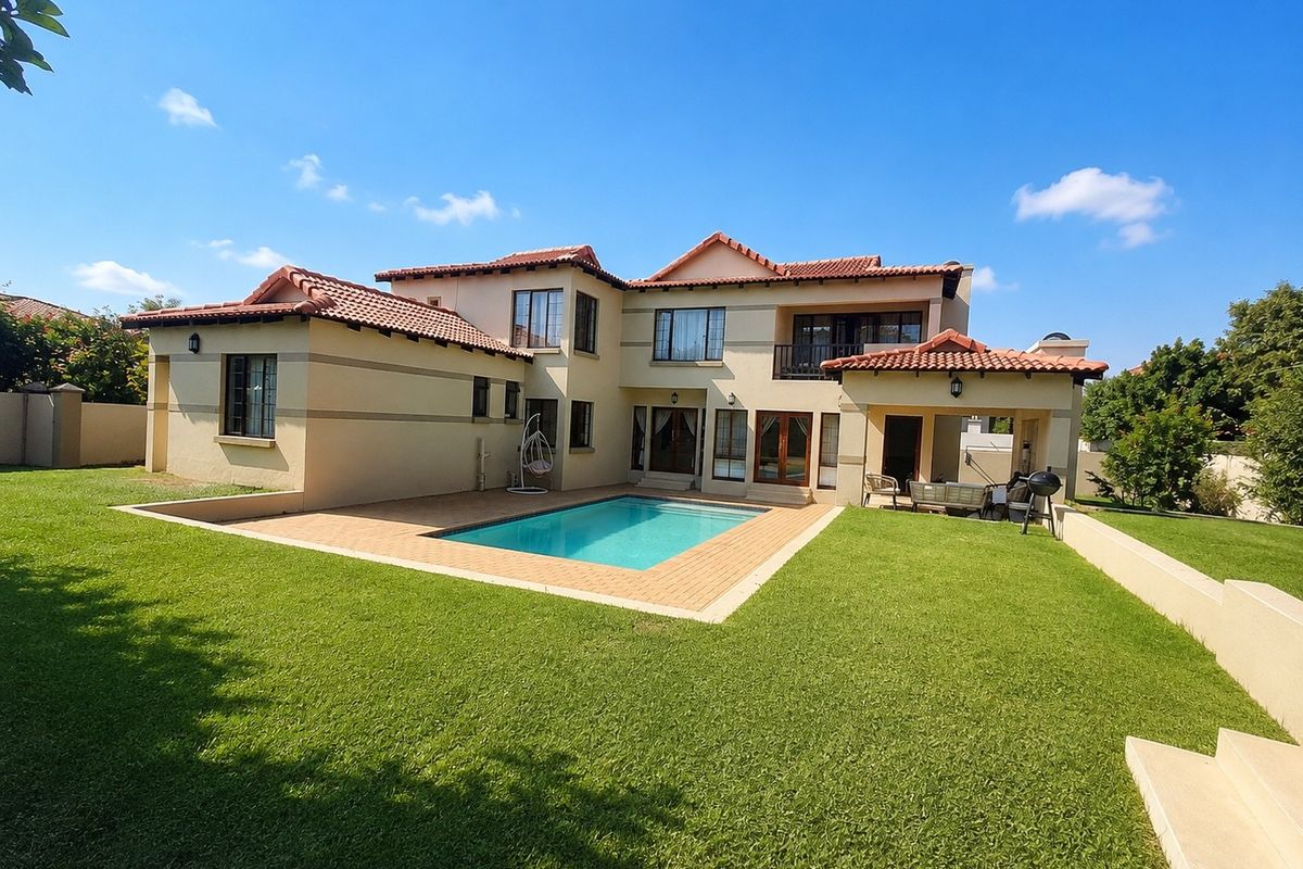 Rear view of a two-story house featuring a swimming pool, paved patio area, balcony, and well-maintained garden lawn.