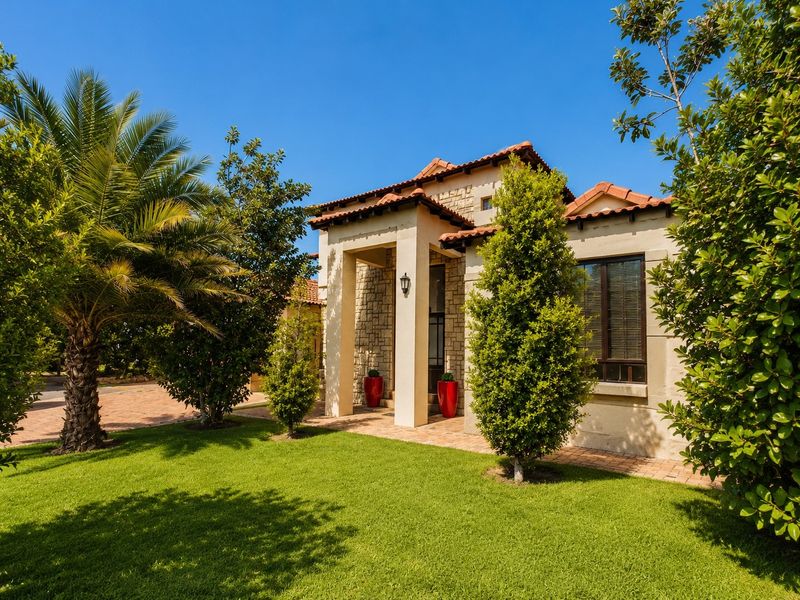 A well-maintained front facade featuring stone cladding, terracotta roof tiles, and a covered entrance porch, set within a landscaped garden.
