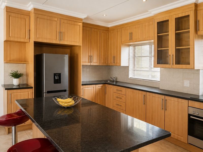 A well-maintained kitchen featuring light wood cabinetry, dark granite countertops, a central island, and integrated stainless steel appliances.