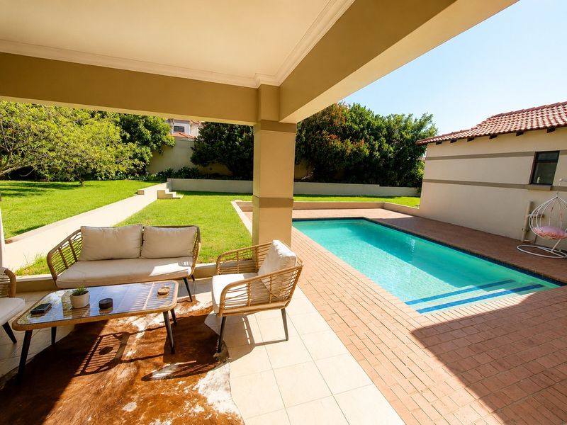 A spacious covered patio overlooking a private swimming pool and well-maintained garden area, perfect for outdoor relaxation and entertainment.