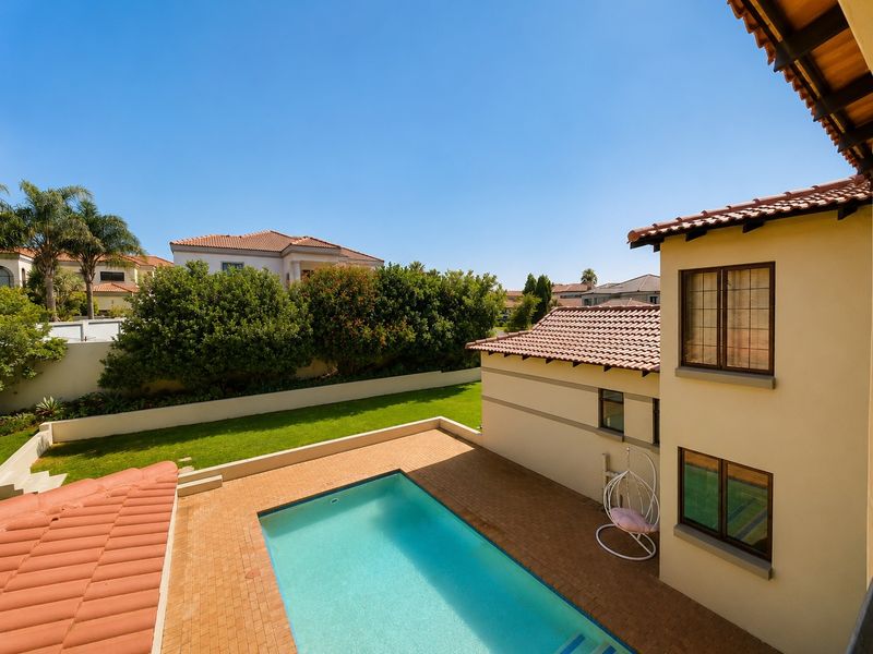 An elevated view of a private backyard featuring a swimming pool, brick-paved patio area, and a well-maintained lawn surrounded by boundary walls.