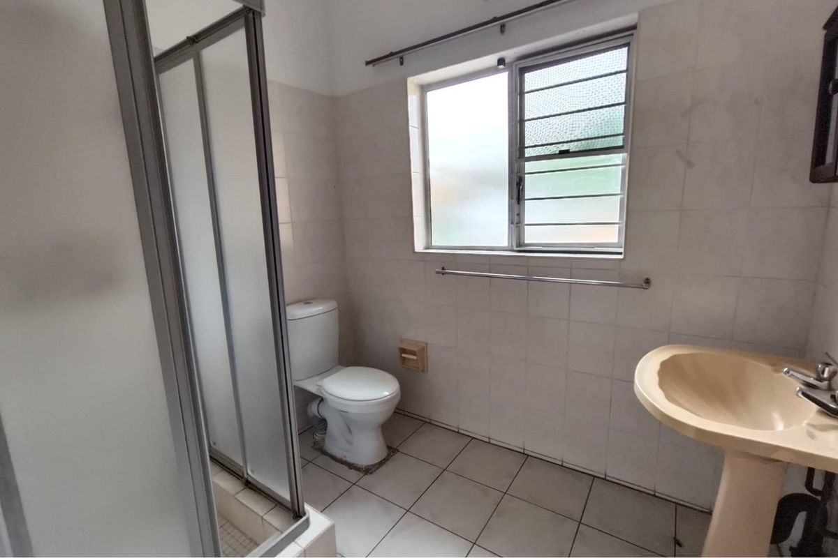 A functional bathroom featuring a shower enclosure, pedestal basin, and toilet, finished with neutral wall and floor tiling.