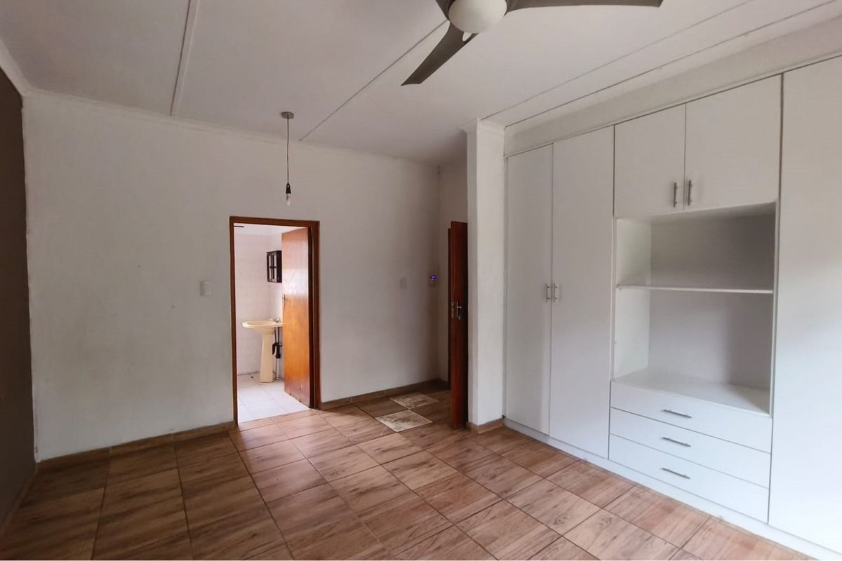 A spacious bedroom featuring built-in cupboards, tiled flooring, and a ceiling fan, with direct access to an adjoining bathroom.