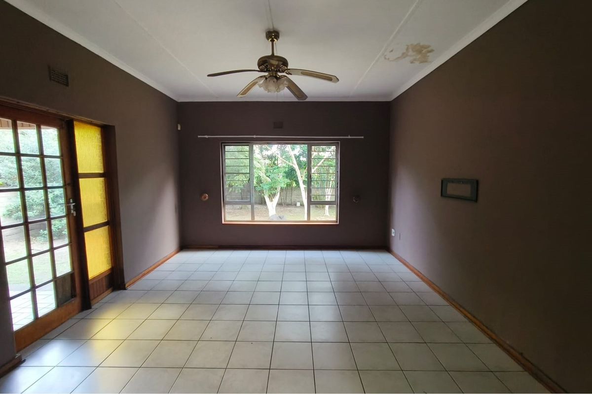 An empty living room featuring tiled flooring, a ceiling fan, and large windows providing natural light and garden views.