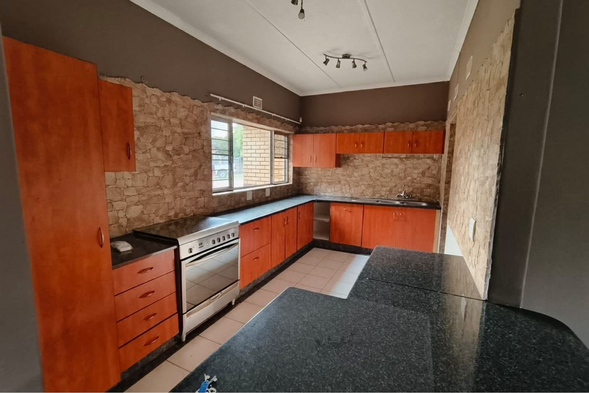 A functional kitchen featuring wooden cabinetry, dark countertops, a freestanding stove, and stone-cladding wall accents, offering a solid foundation for a modern renovation.