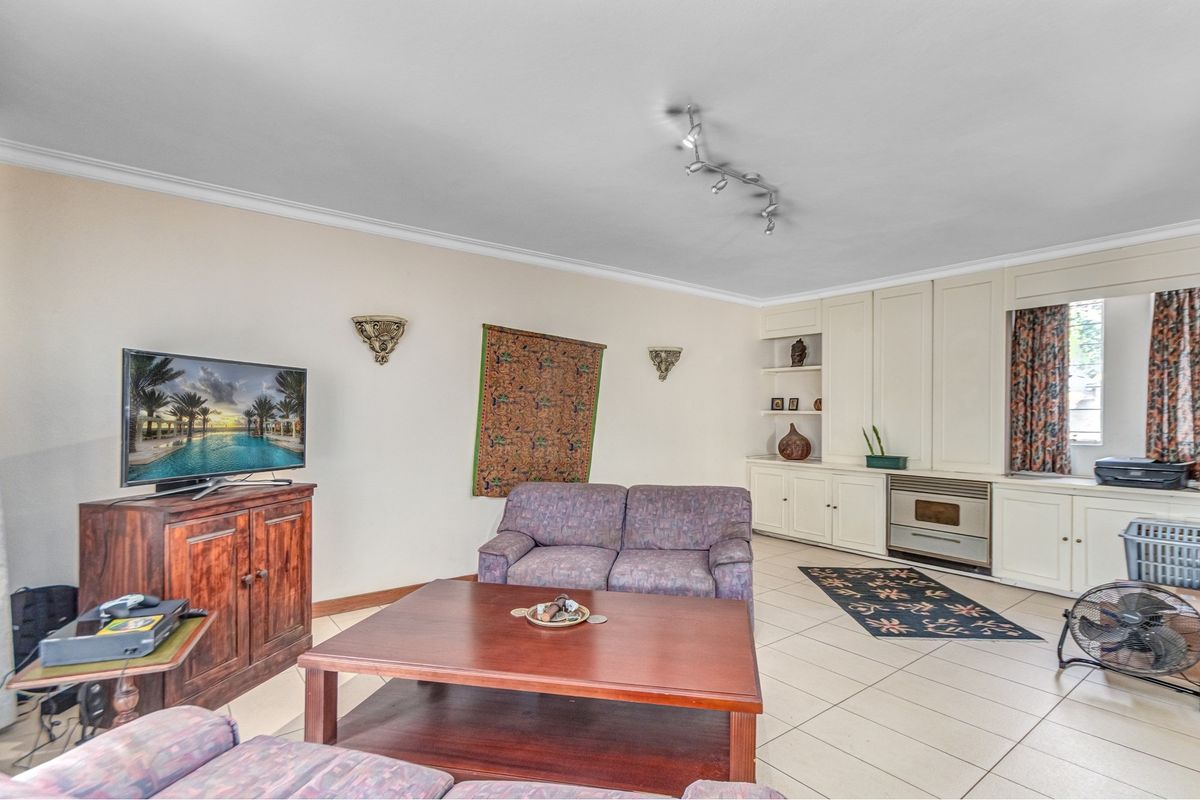 A spacious living room featuring neutral ceramic floor tiles, coving, and extensive built-in cabinetry with an integrated oven.