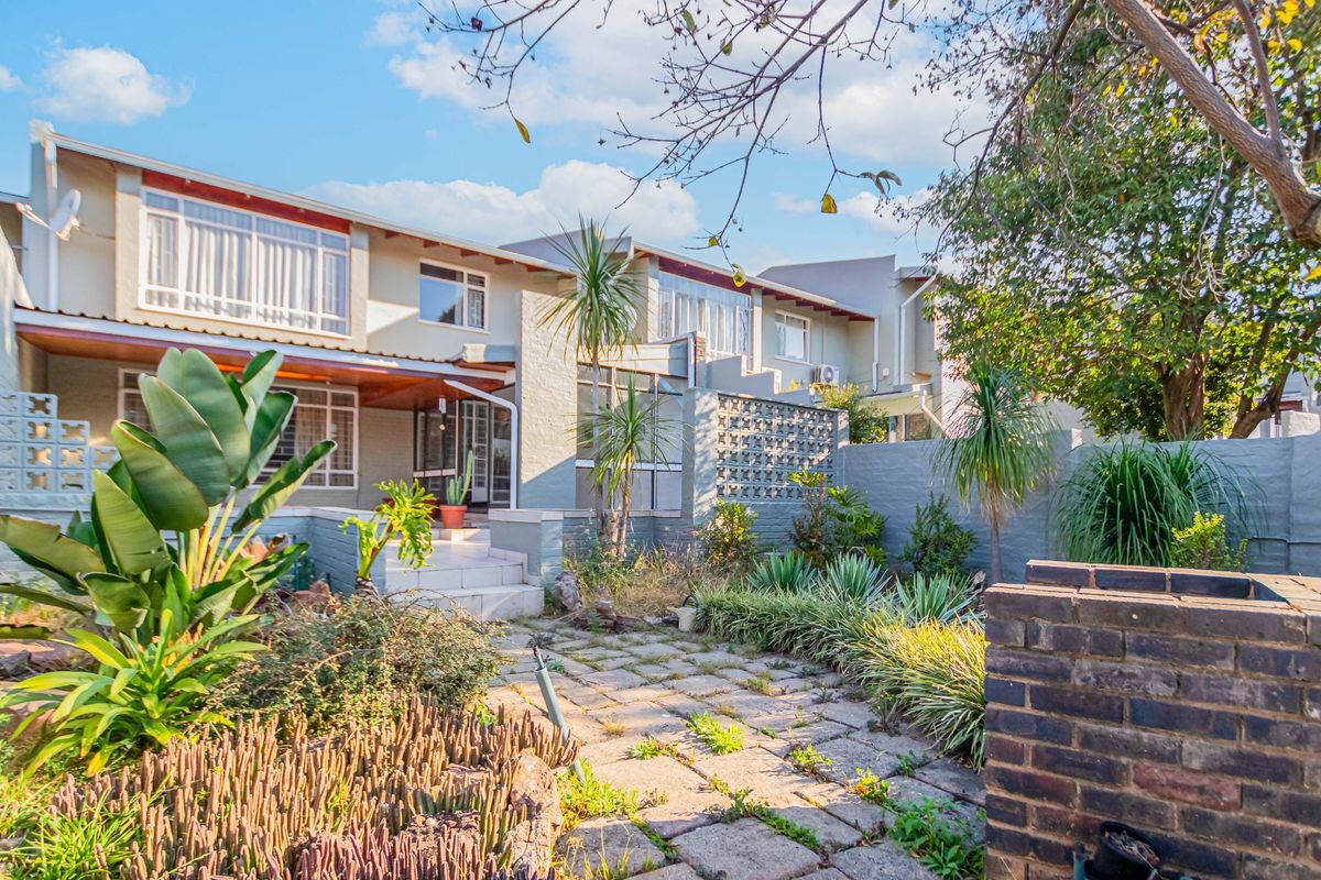 Rear exterior view of the townhouse featuring a paved patio area, covered porch, and established garden with brick boundary walls.