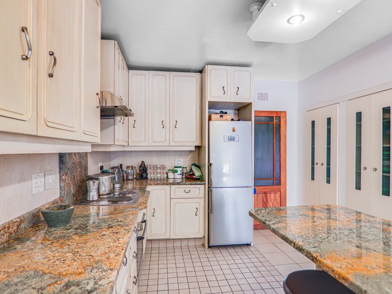A functional kitchen featuring granite countertops, built-in cabinetry, an electric hob with extractor, and tiled flooring with integrated pantry storage.