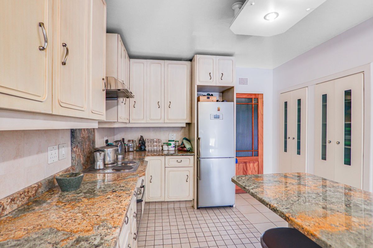 A functional kitchen featuring granite countertops, built-in cabinetry, an electric hob with extractor, and tiled flooring with integrated pantry storage.