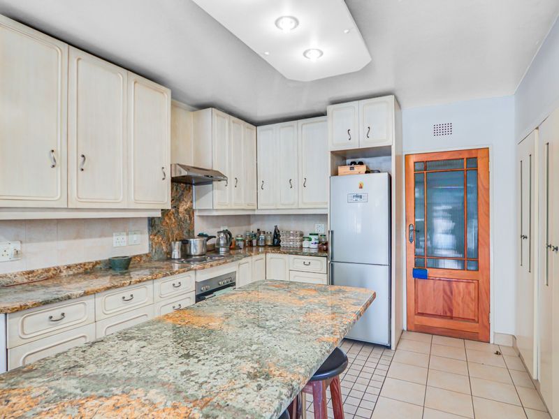 A functional kitchen featuring granite countertops, built-in cabinetry, an integrated oven and hob, and tiled flooring, with a classic timber door leading outside.