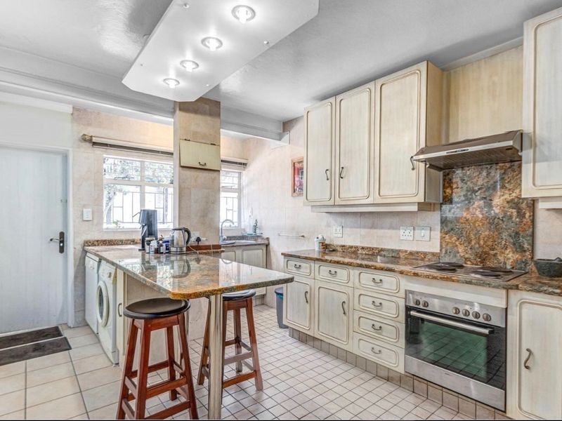 Functional kitchen featuring granite countertops, built-in oven, electric hob, extractor fan, and ample cabinetry with a breakfast bar area.