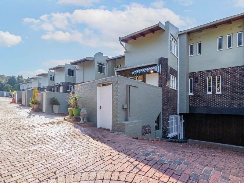 Front elevation of a townhouse complex featuring a brick paved driveway, multi-level facade with brick and painted masonry finishes, and integrated garage access.