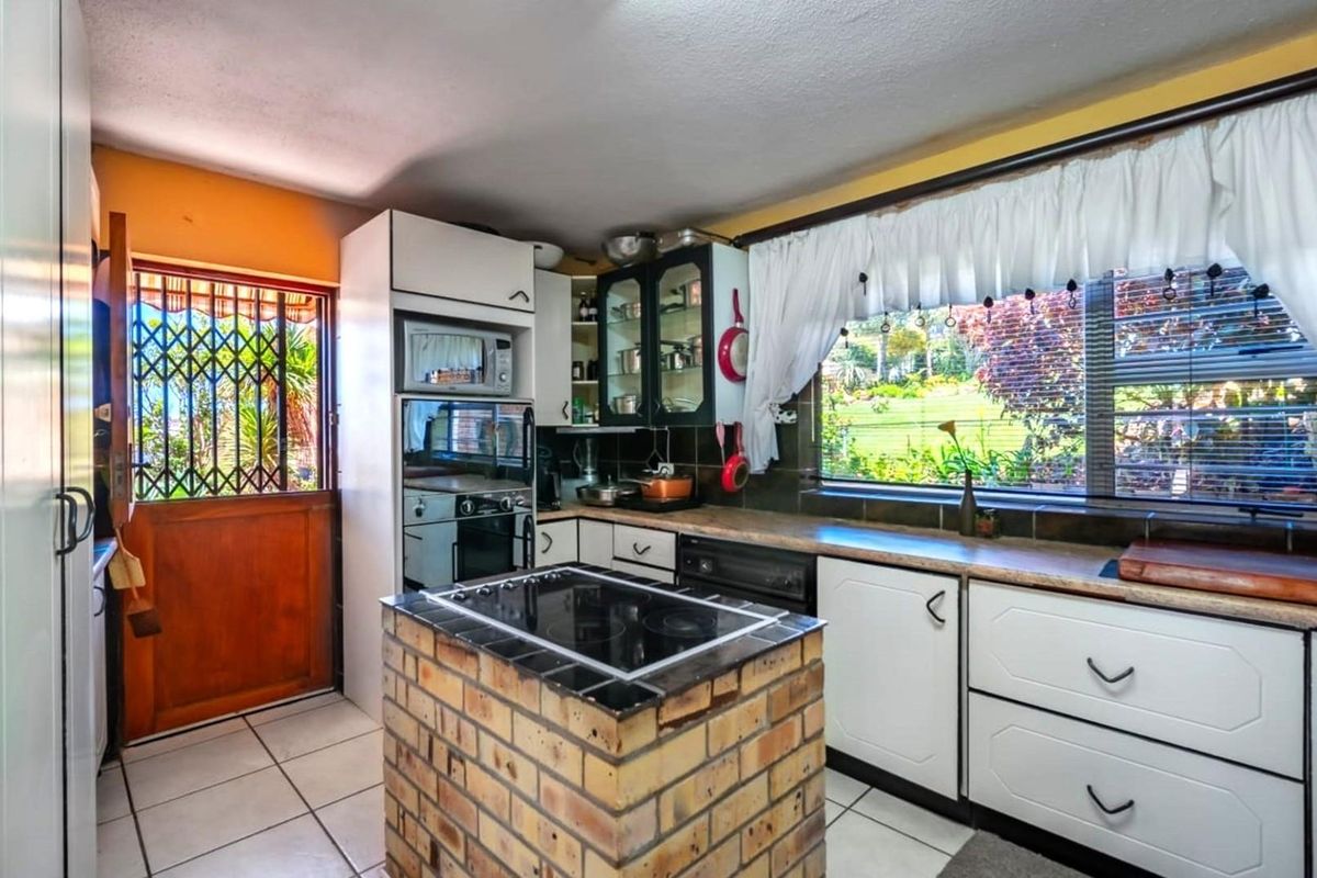 A functional kitchen featuring a central brick-base island with a built-in cooktop, white cabinetry, and direct access to the exterior.