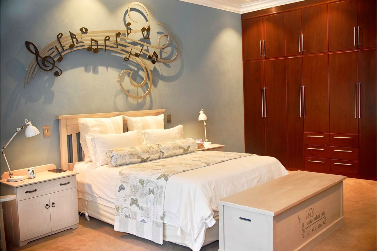 A well-maintained bedroom featuring extensive dark wood built-in cupboards, recessed ceiling lighting, and decorative coving.