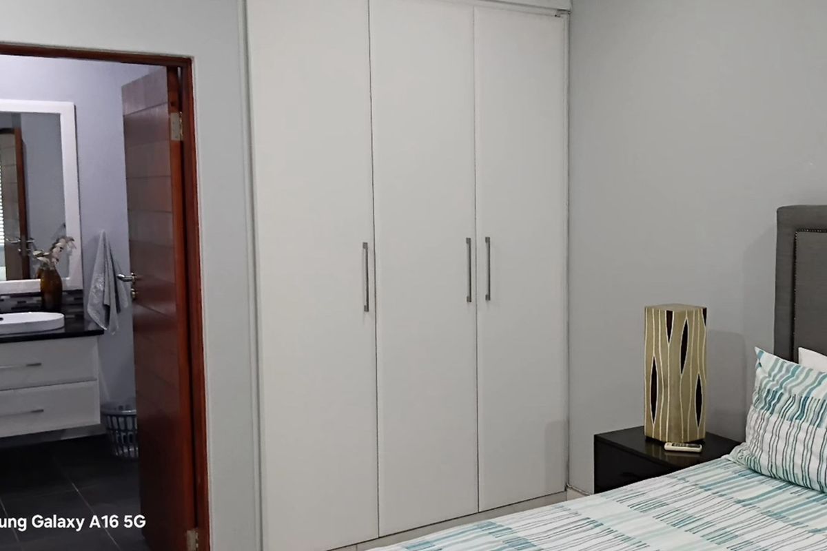 A bedroom featuring built-in white cabinetry and an adjoining en-suite bathroom with a modern vanity and mirror.