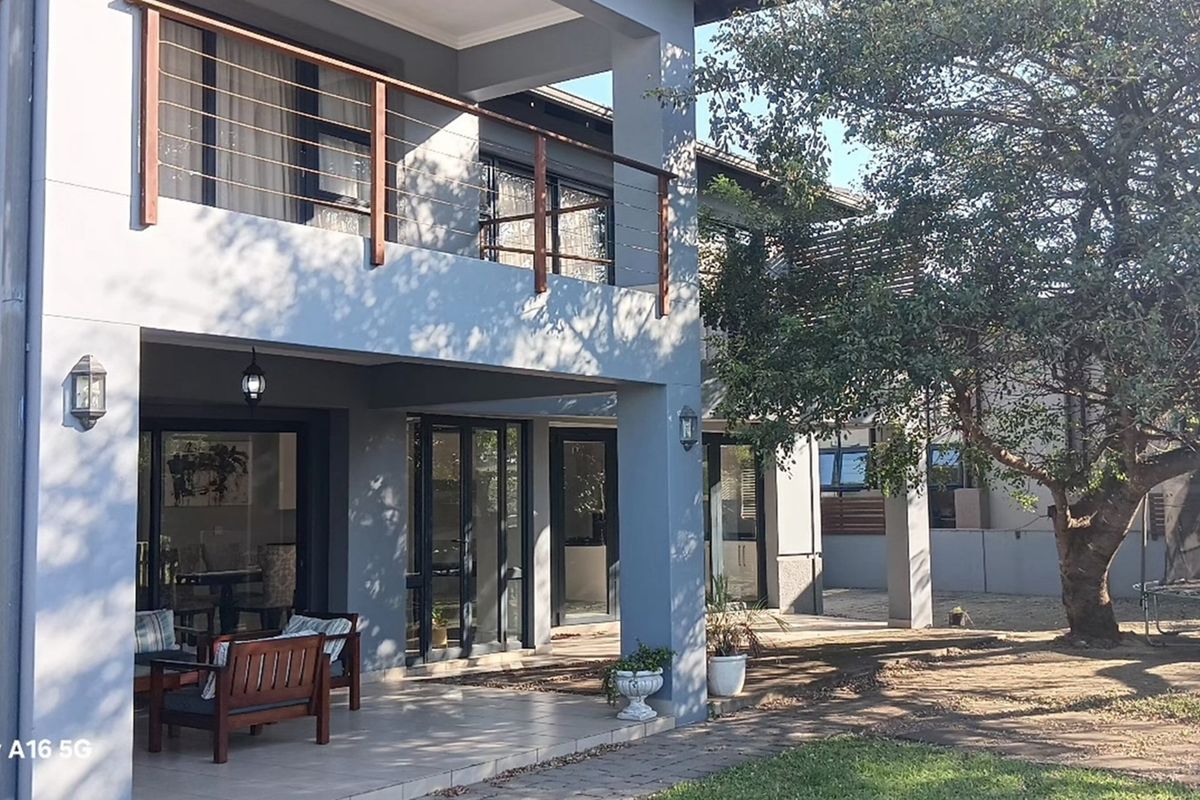 A modern double-story home featuring a covered ground-floor patio, an upper-level balcony with timber railings, and large glass sliding doors.