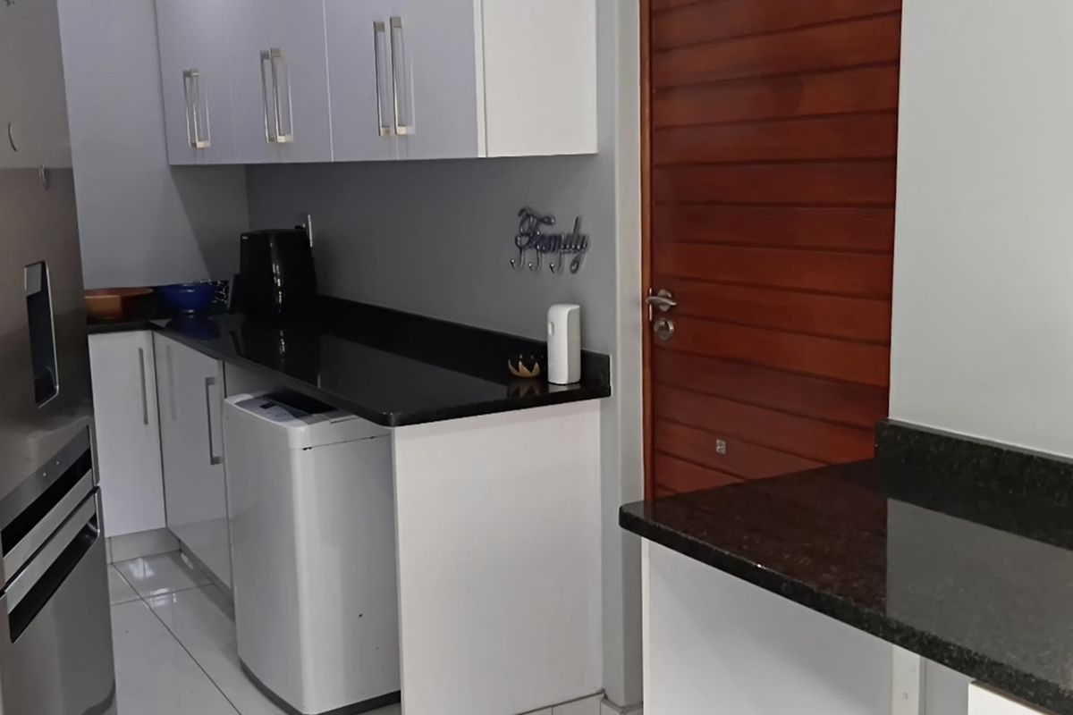 A functional kitchen area featuring modern white cabinetry, contrasting black granite countertops, and tiled flooring, adjacent to a wooden door.