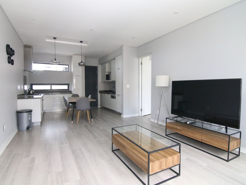 Modern open-plan living area featuring a sleek kitchen with built-in cabinetry, integrated appliances, and light wood-look flooring throughout.