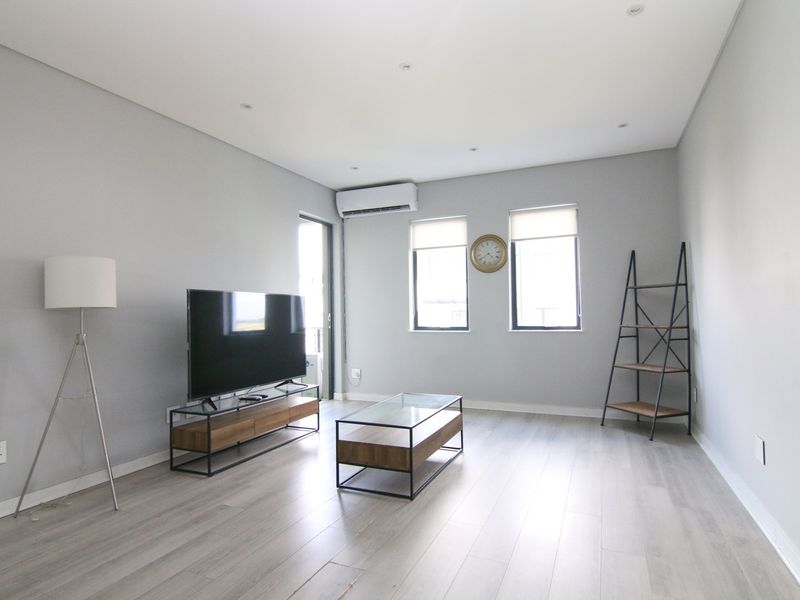 A bright and modern living room featuring light wood-look flooring, recessed ceiling lighting, and a wall-mounted air conditioning unit.
