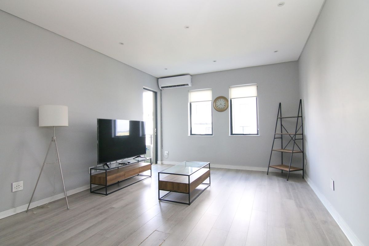 A bright and modern living room featuring light wood-look flooring, recessed ceiling lighting, and a wall-mounted air conditioning unit.
