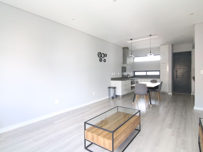 Modern open-plan living area featuring a sleek kitchen with built-in cabinetry, stainless steel extractor fan, and light wood-look flooring throughout.