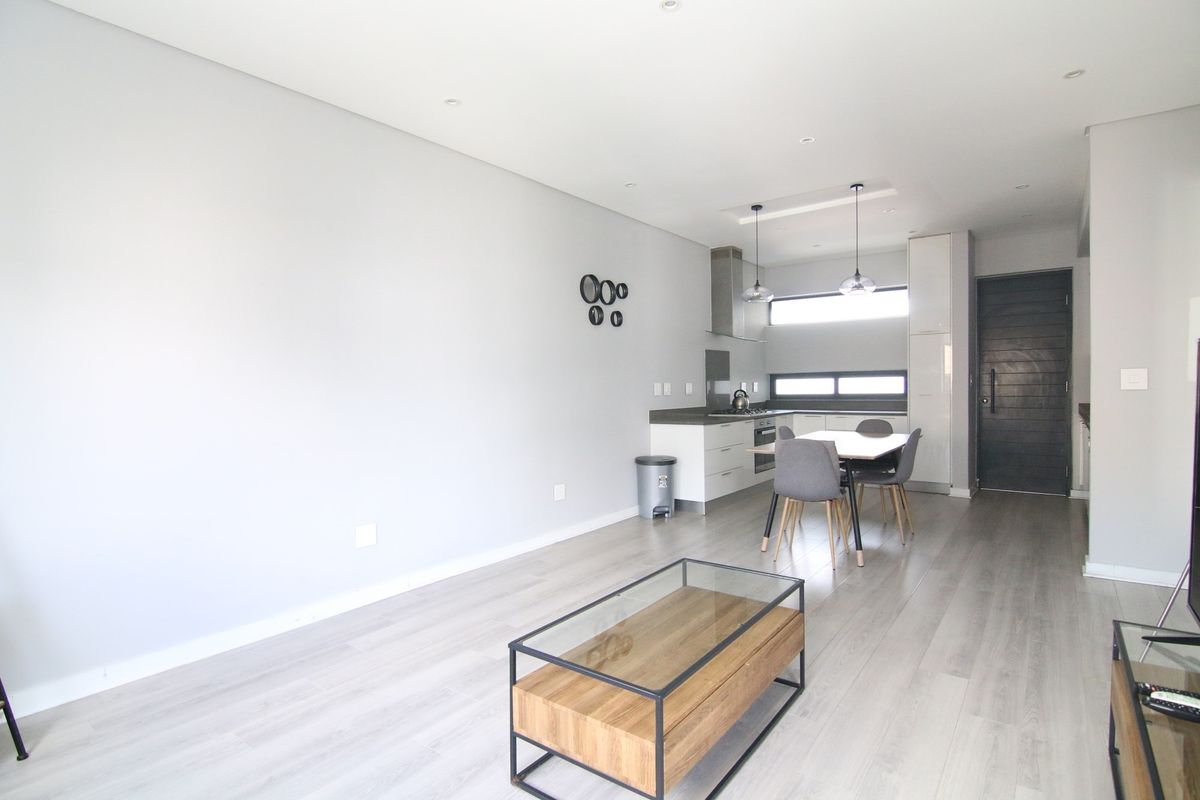 Modern open-plan living area featuring a sleek kitchen with built-in cabinetry, stainless steel extractor fan, and light wood-look flooring throughout.