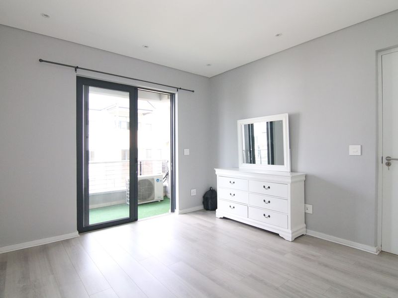A bright bedroom featuring light wood-look flooring, recessed ceiling lighting, and a sliding glass door providing access to a private balcony.